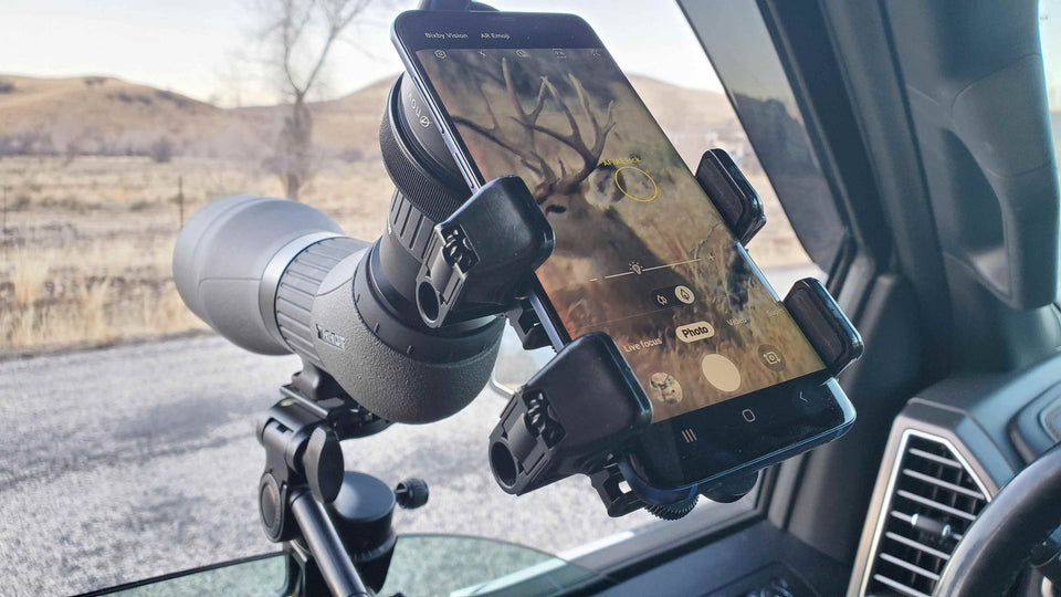 Spotting scope with a smartphone held by a Double Gripper on a car dashboard, viewing a deer